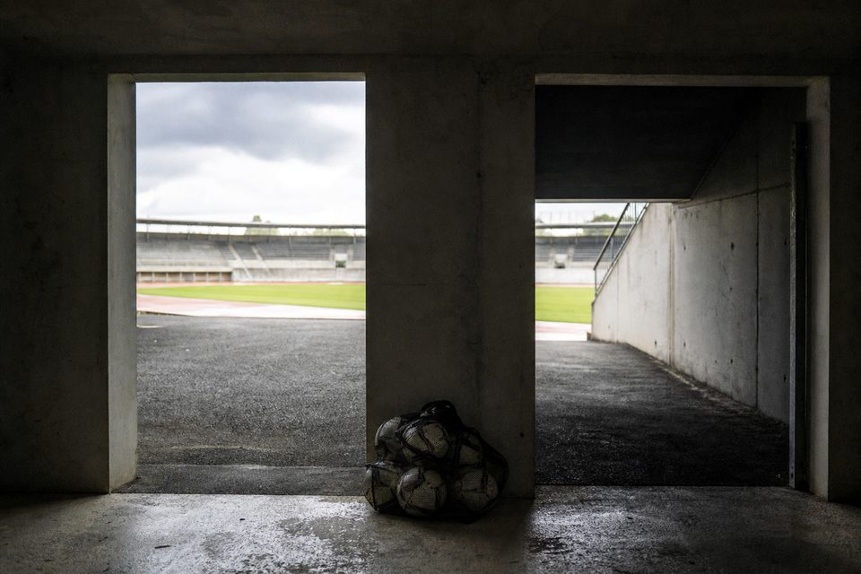 Zdjęcie: dwa sąsiednie betonowe wyjścia z tunelu stadionowego, jedno w świetle dnia, drugie w cieniu, między nimi siatka na piłki. (obraz wygenerowany przez AI)