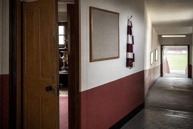 Zdjęcie: lekko uchylone drewniane drzwi klubowego biura, pusta tablica ogłoszeń i szalik na haku, korytarz prowadzi do oświetlonego tunelu. (obraz wygenerowany przez AI)