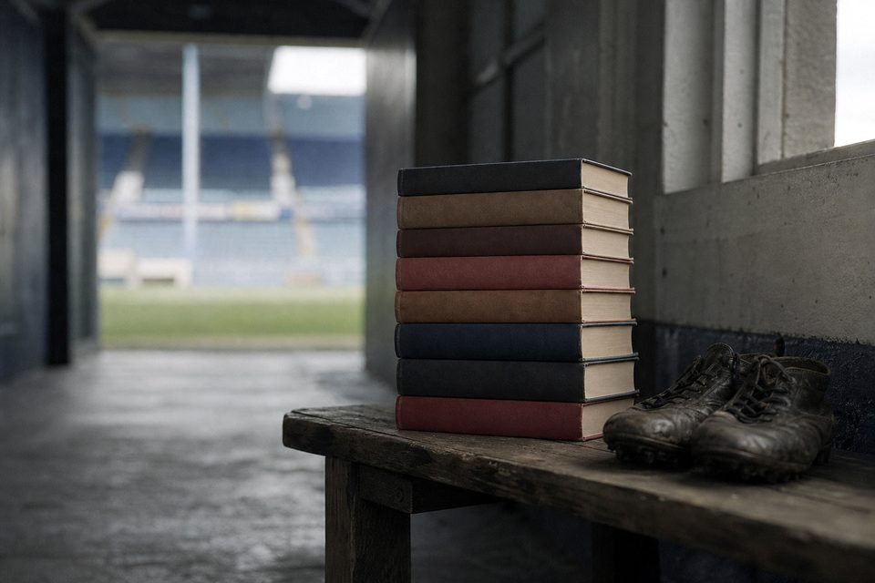 Zdjęcie: stos jednolitych twardookładkowych tomów bez napisów na drewnianej ławce w tunelu stadionowym, obok para zniszczonych butów. (obraz wygenerowany przez AI)